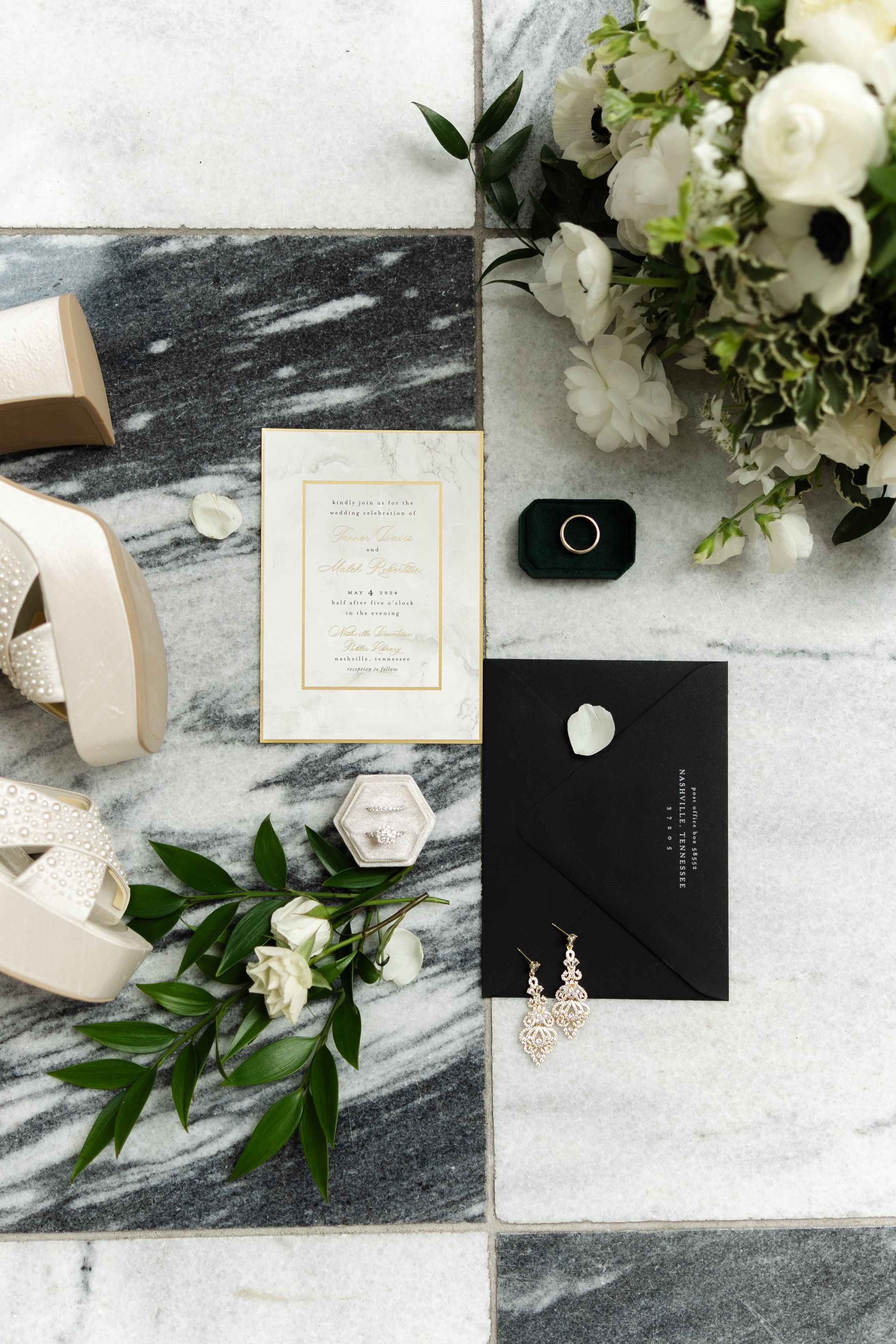 Elegant wedding stationery flatlay with black envelopes, white flowers, and ribbon on marble surface.
