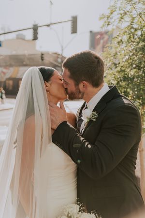Bride and groom sharing first kiss outdoors on wedding day in urban setting.