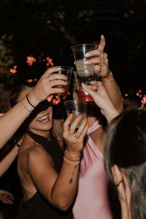 Group of women toasting with plastic cups at outdoor evening celebration party.