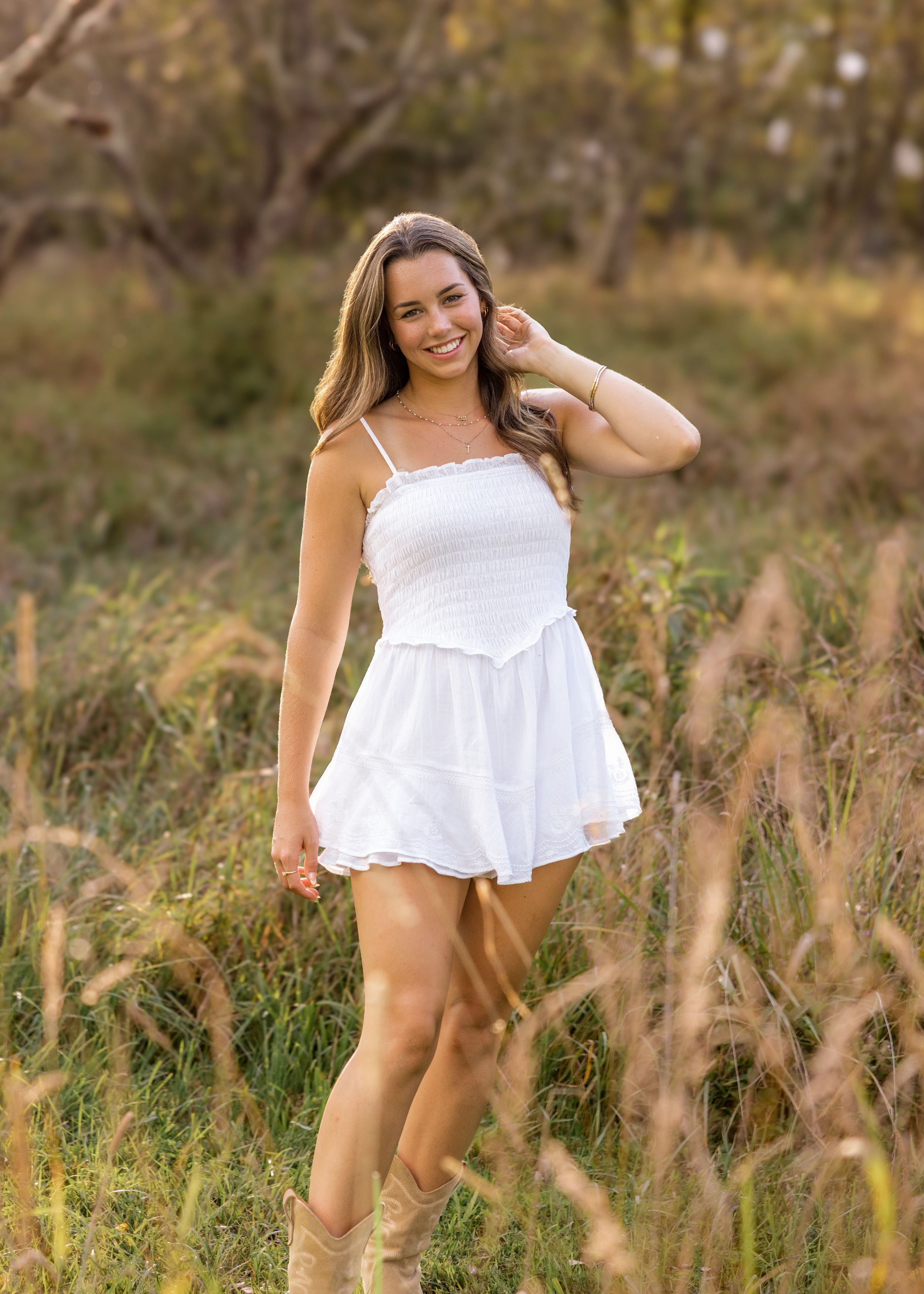 Playful outdoor portrait series in a white summer dress among tall grass at golden hour.