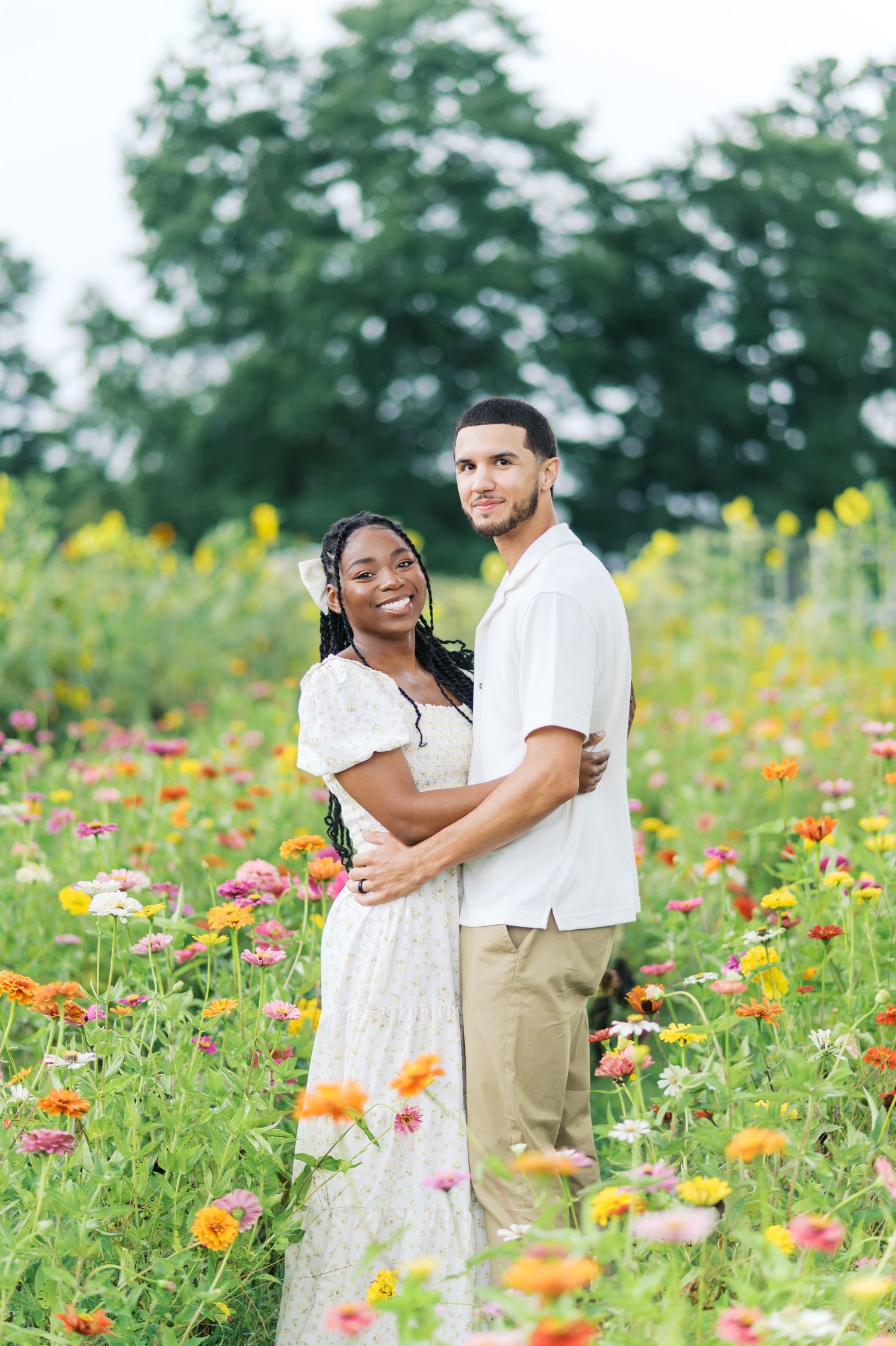 A couple shares a romantic moment in a vibrant wildflower field with orange and pink blooms on a sunny summer day.