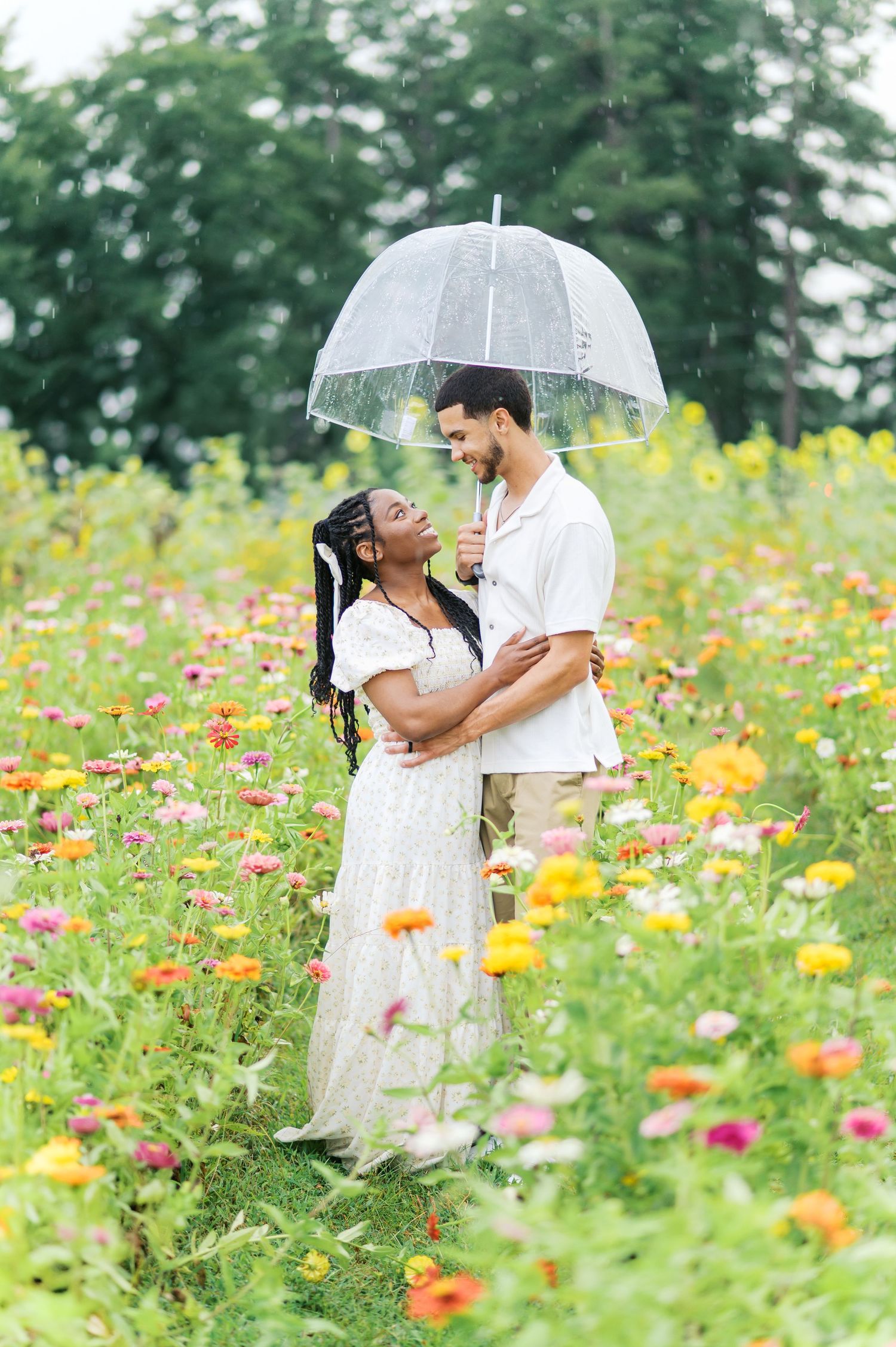 A couple shares a romantic moment under a clear umbrella in a vibrant wildflower meadow on a summer day.