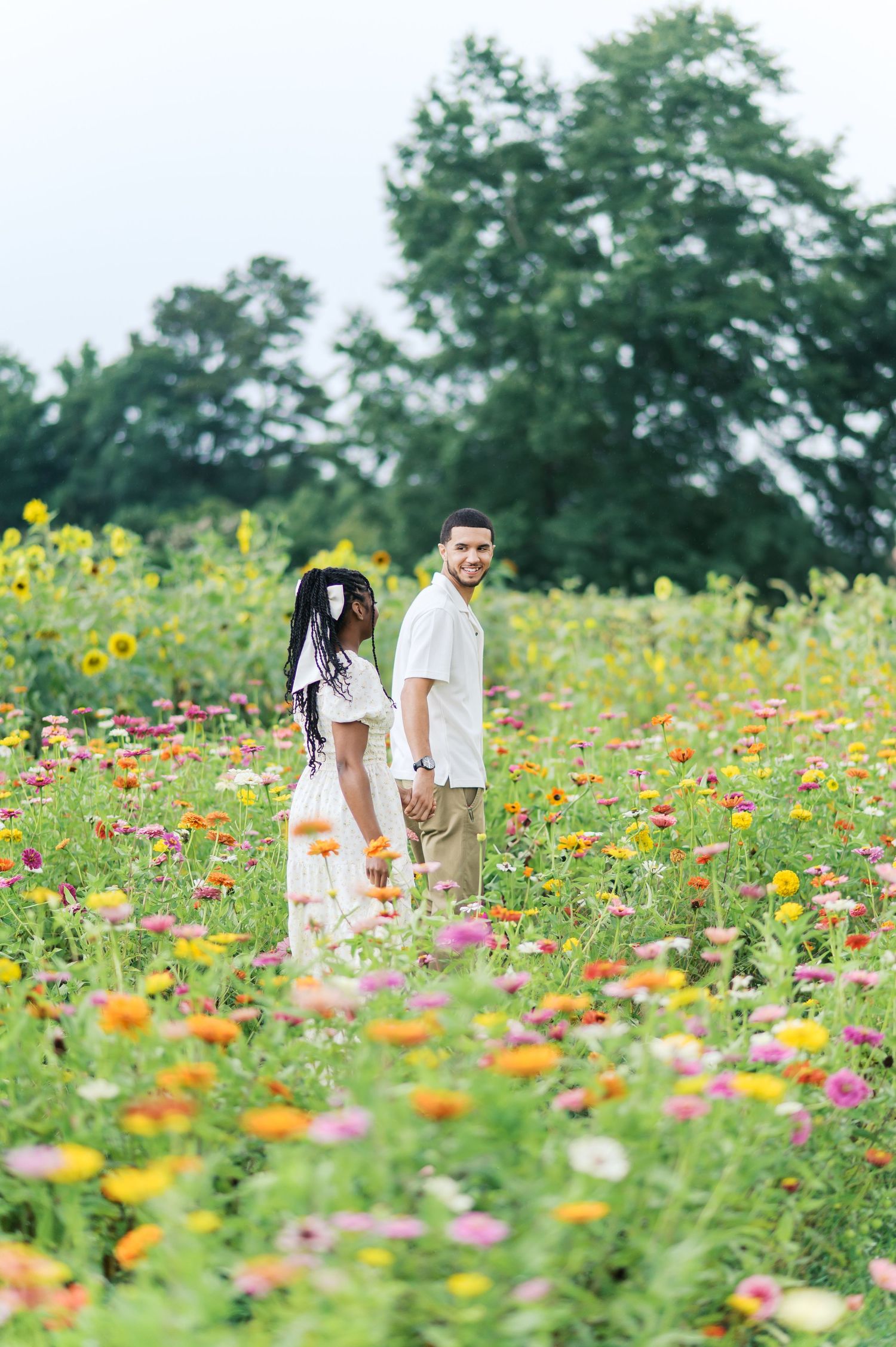 Couple walking through vibrant flower field filled with colorful pink, orange and yellow blooms on a summer day.