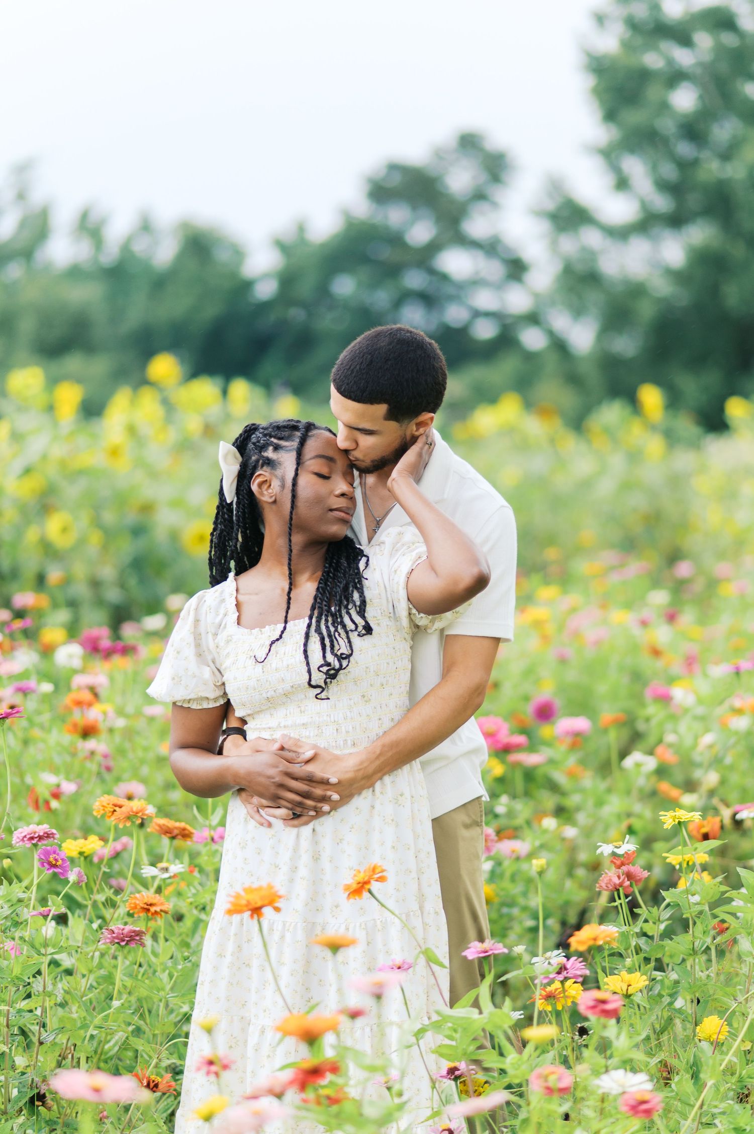 A romantic couple embraces in a vibrant wildflower field filled with colorful zinnias and yellow blooms on a summer day.
