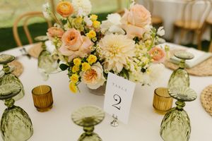 Elegant wedding table centerpiece with peach roses, dahlias, yellow flowers and amber glassware on white tablecloth.