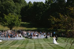 Panoramic view of an outdoor garden wedding ceremony with white chairs arranged on a manicured lawn surrounded by trees.