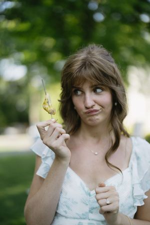 5 photos of someone in a white ruffled dress making playful faces while holding up a butterfly in a garden.