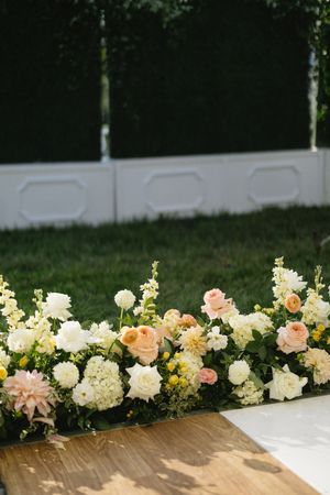 Elegant floral arrangement with peach and white roses, hydrangeas and snapdragons decorating a wooden surface outdoors.