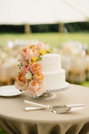 A white wedding cake adorned with delicate peach and yellow flowers sits elegantly on a cake stand.