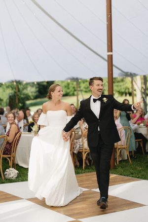A joyful wedding couple shares their first dance on a wooden floor under an elegant white tent during their reception celebration.