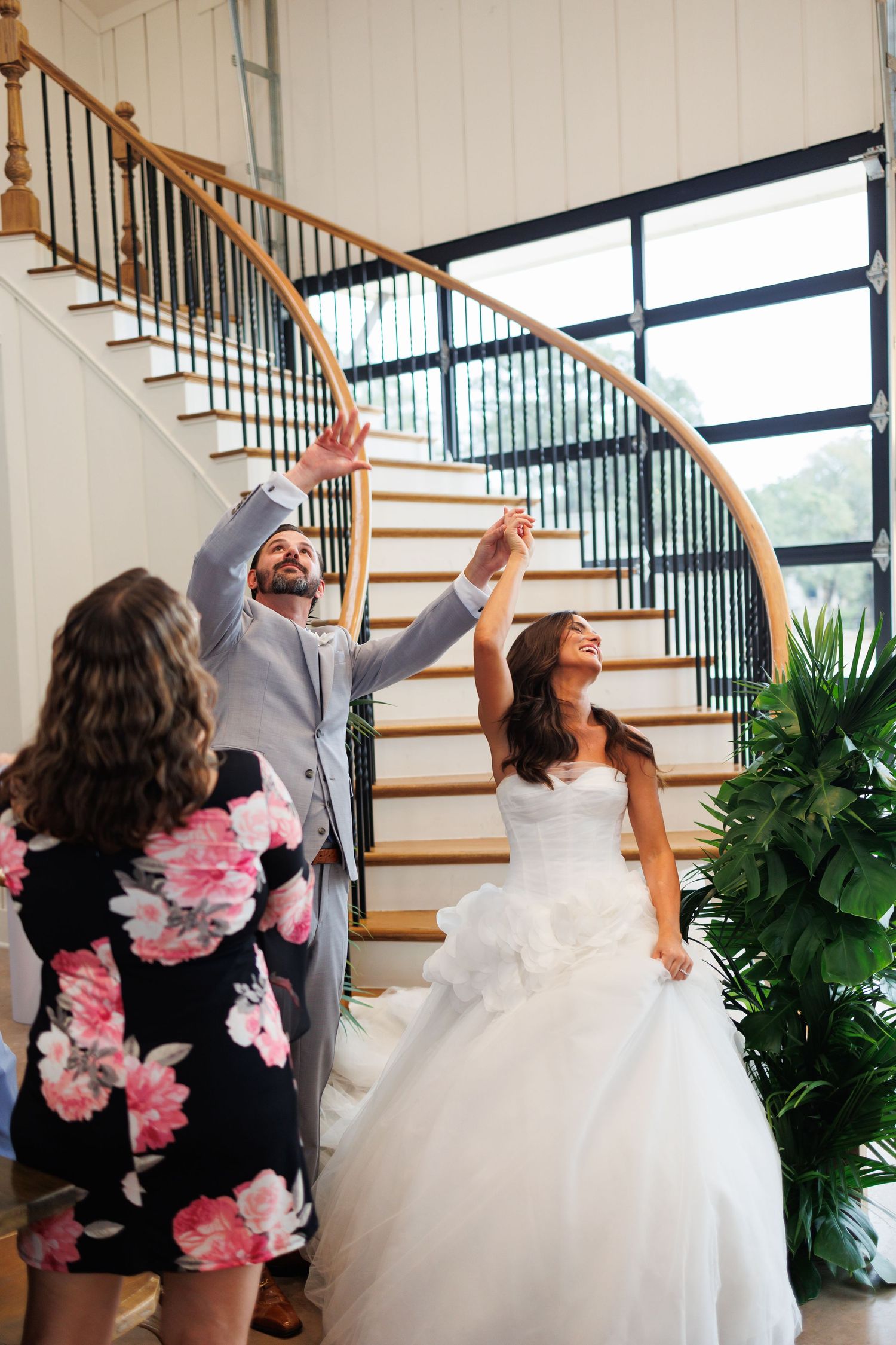 Couple enters their wedding reception by a grand curved staircase with iron railings and indoor plants at Bella Cavalli