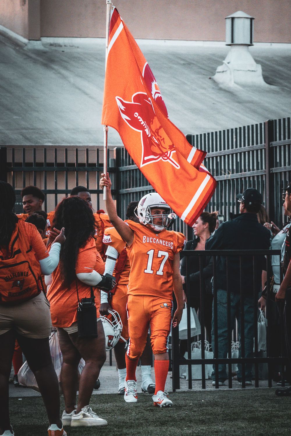 Team carrying orange flags and walking along field fence before game.