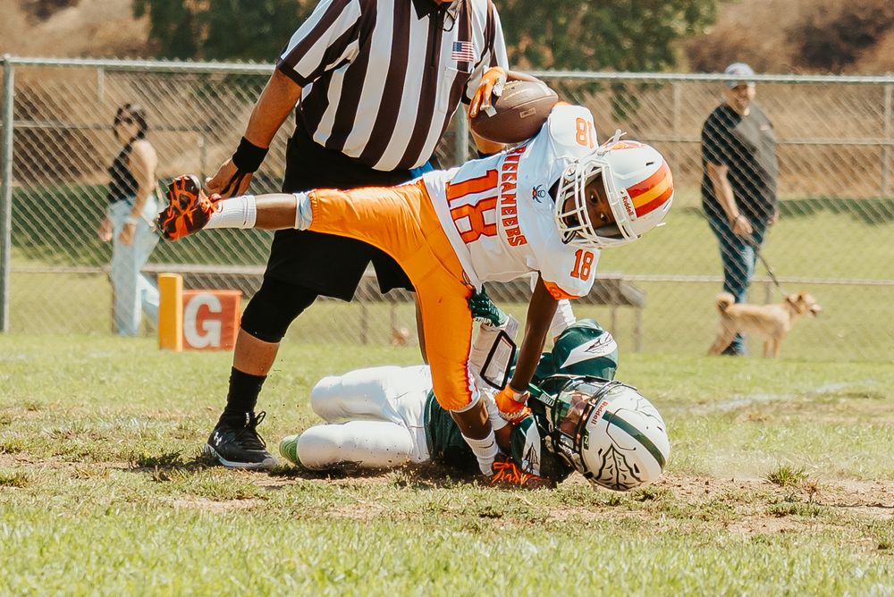 Football players collide during a tackle on a grassy field with referees observing the play.