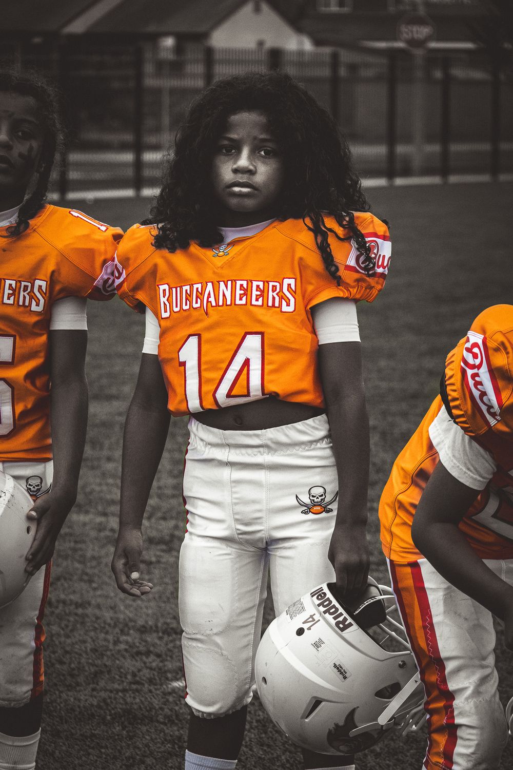 Youth football players in orange Buccaneers jerseys posing with helmets in black and white.
