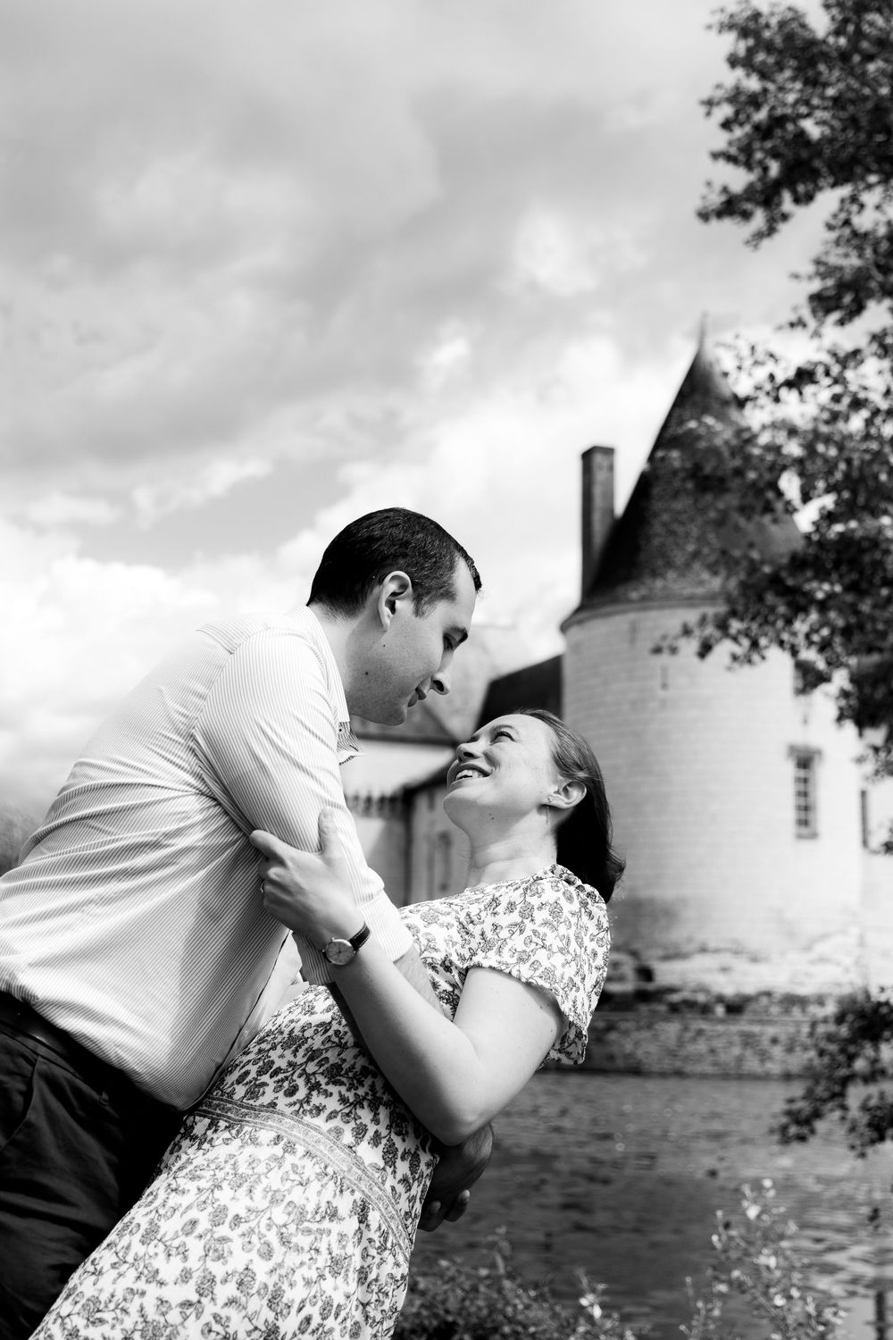 Black and white photo of couple dancing and laughing in front of a historic French chateau.