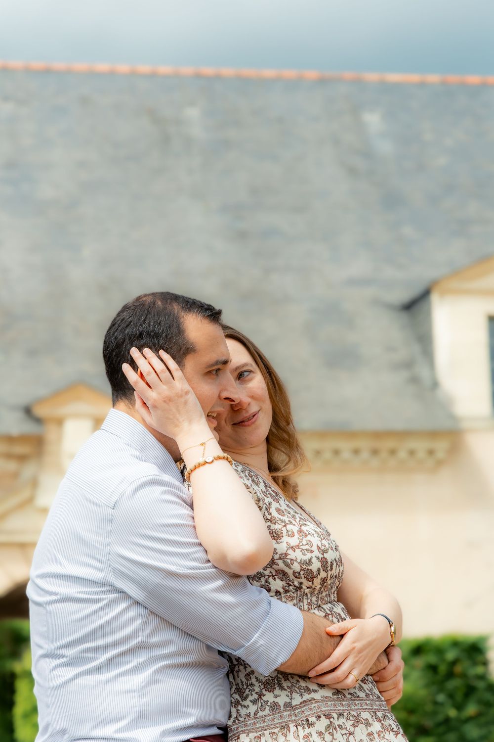 Couple embracing outdoors near a French château, woman smiling warmly while holding man's face.