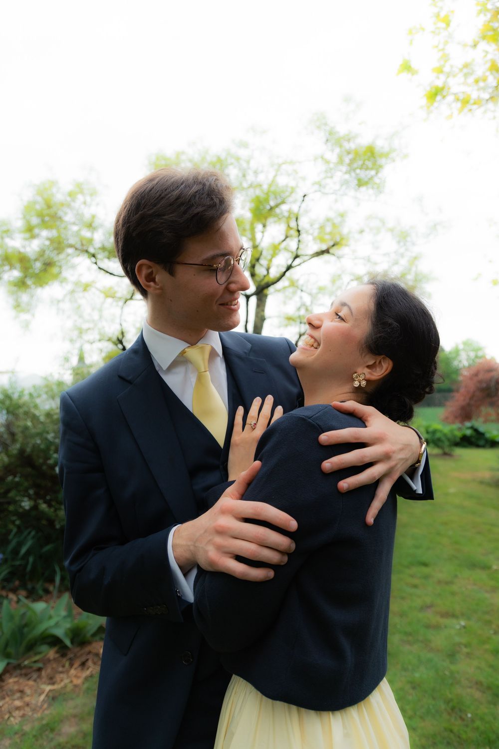 Happy couple in formal wear embracing in a lush green garden, man in navy suit with yellow tie.