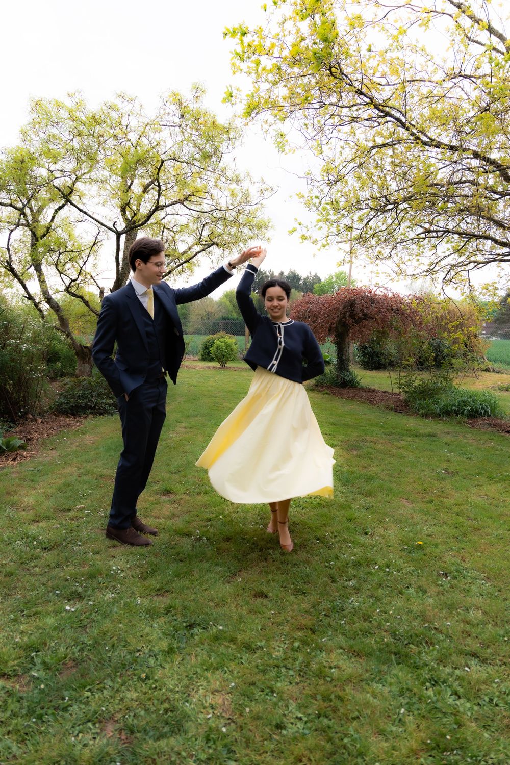 Joyful couple dancing outdoors in a garden, woman in flowing yellow skirt spinning elegantly.