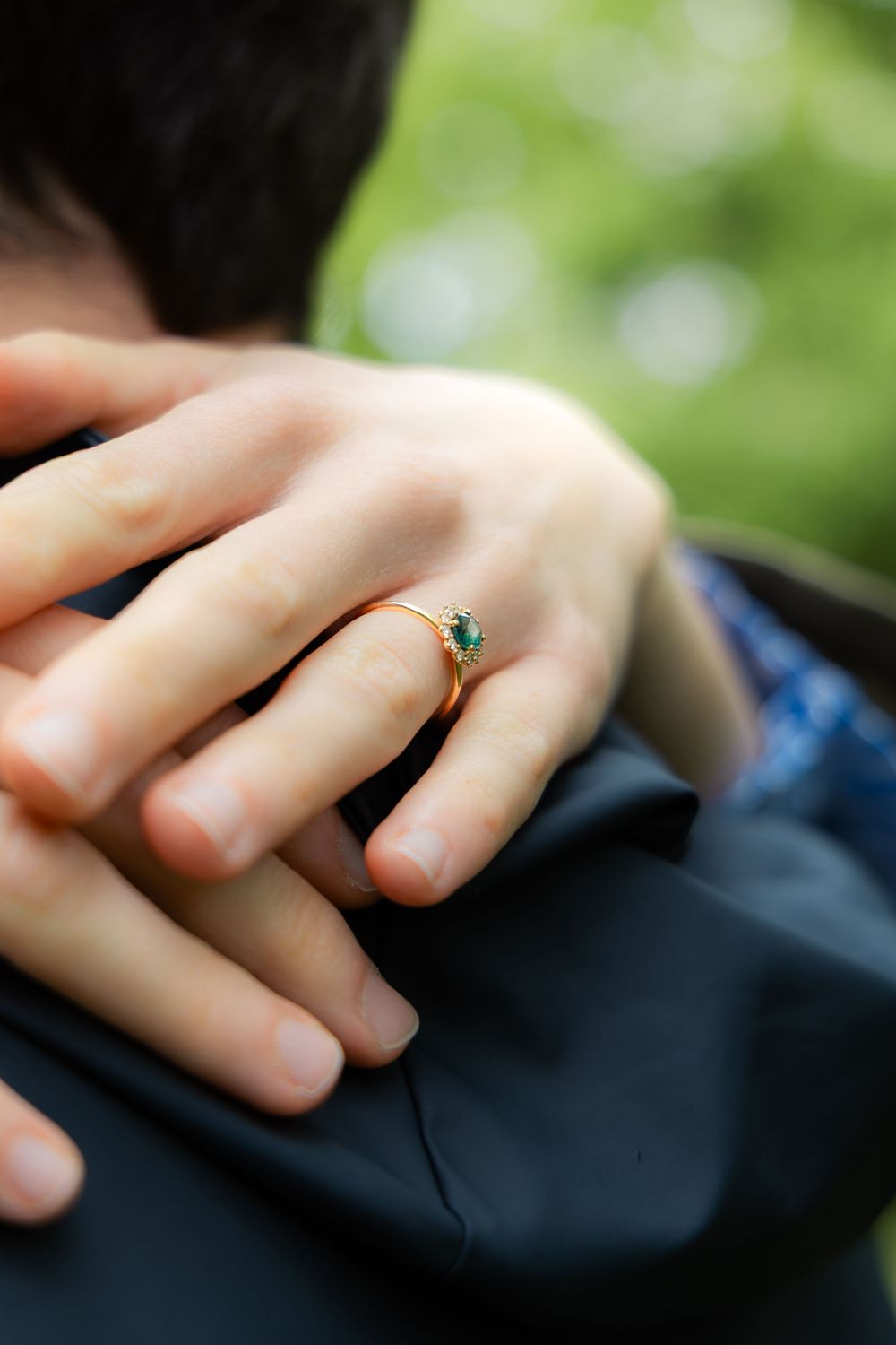 Close-up of a woman's hand wearing a gold engagement ring with green emerald stone.