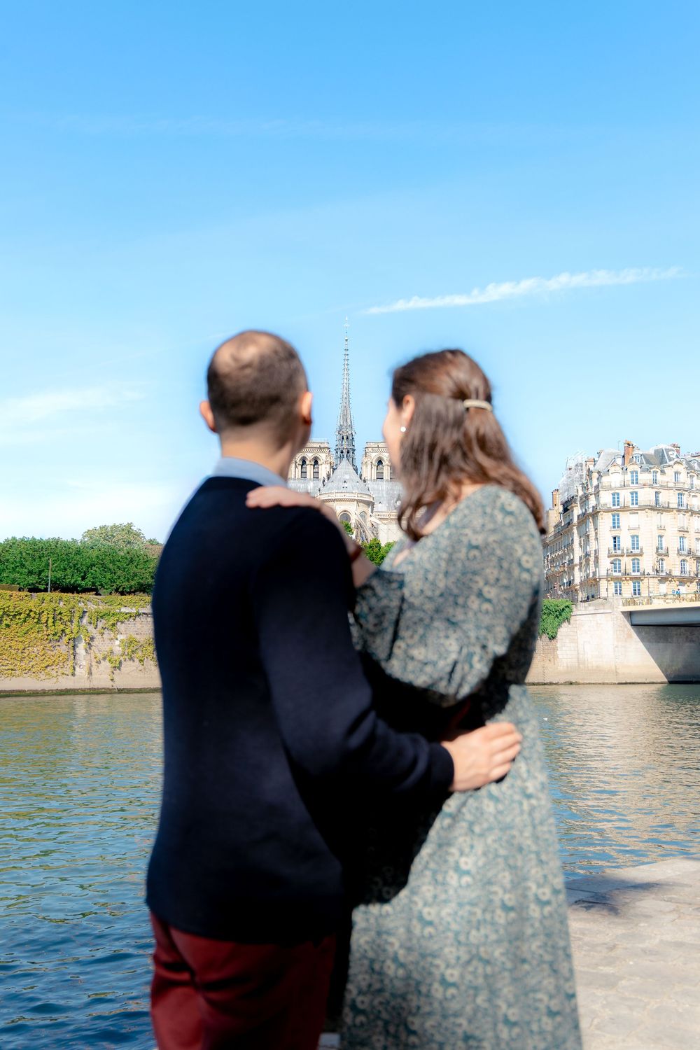 Couple embracing while gazing at Notre-Dame Cathedral from the banks of the Seine River in Paris.
