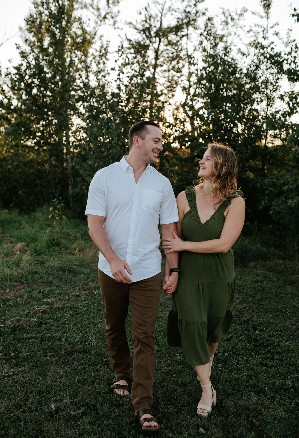 A couple walking together at sunset in a natural outdoor setting, with green trees in the background.