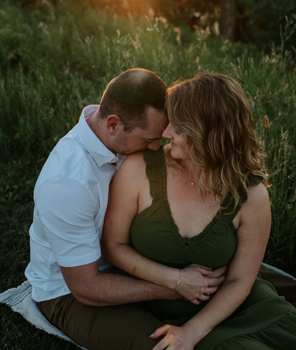 Intimate couple sharing tender moments in a grassy outdoor setting at dusk.
