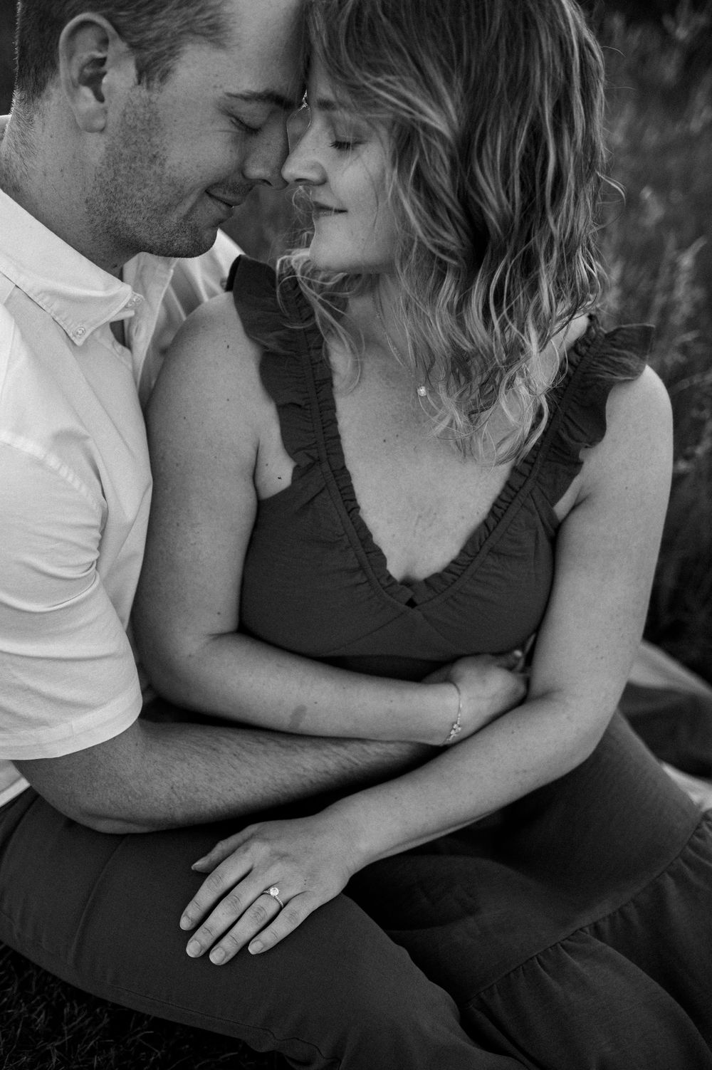 Intimate black and white portrait of couple nuzzling close together against blurred background.