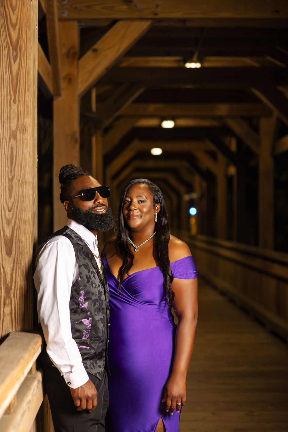 A couple shares a joyful moment in formal attire inside a wooden covered bridge.