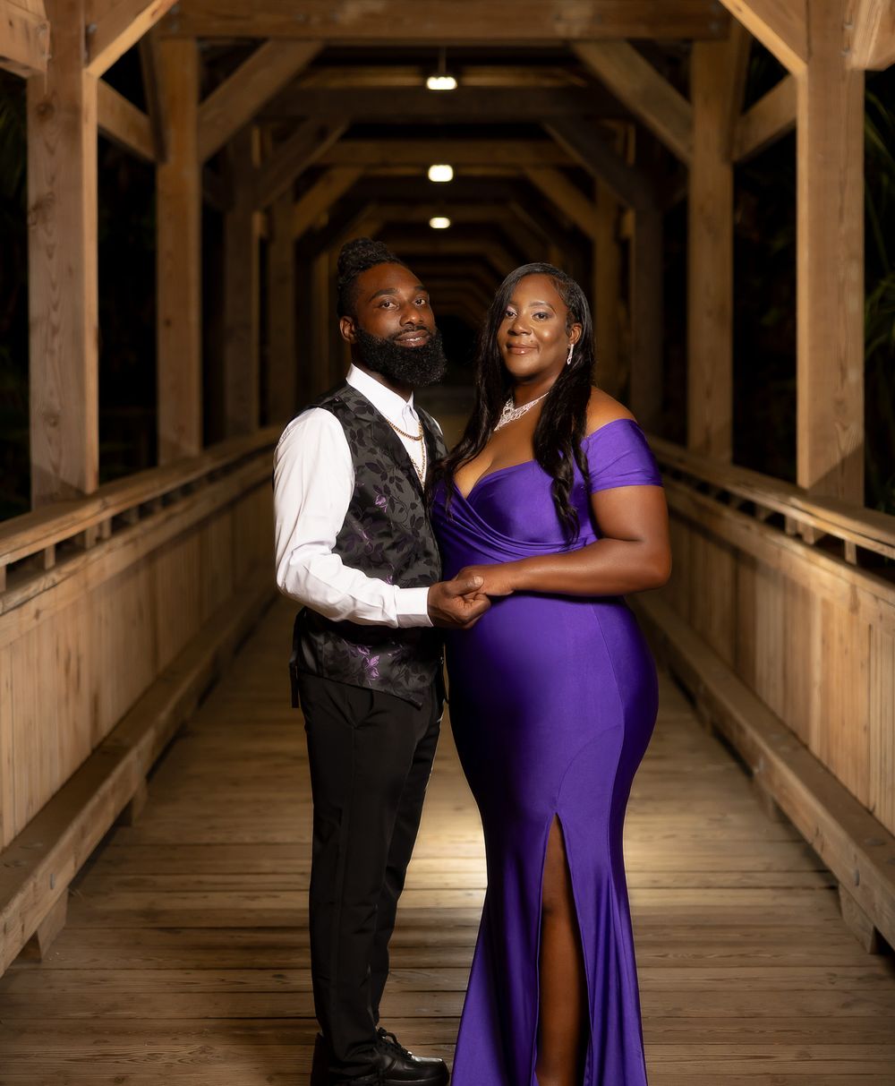 A formal portrait of a couple standing in an atmospheric wooden covered walkway.