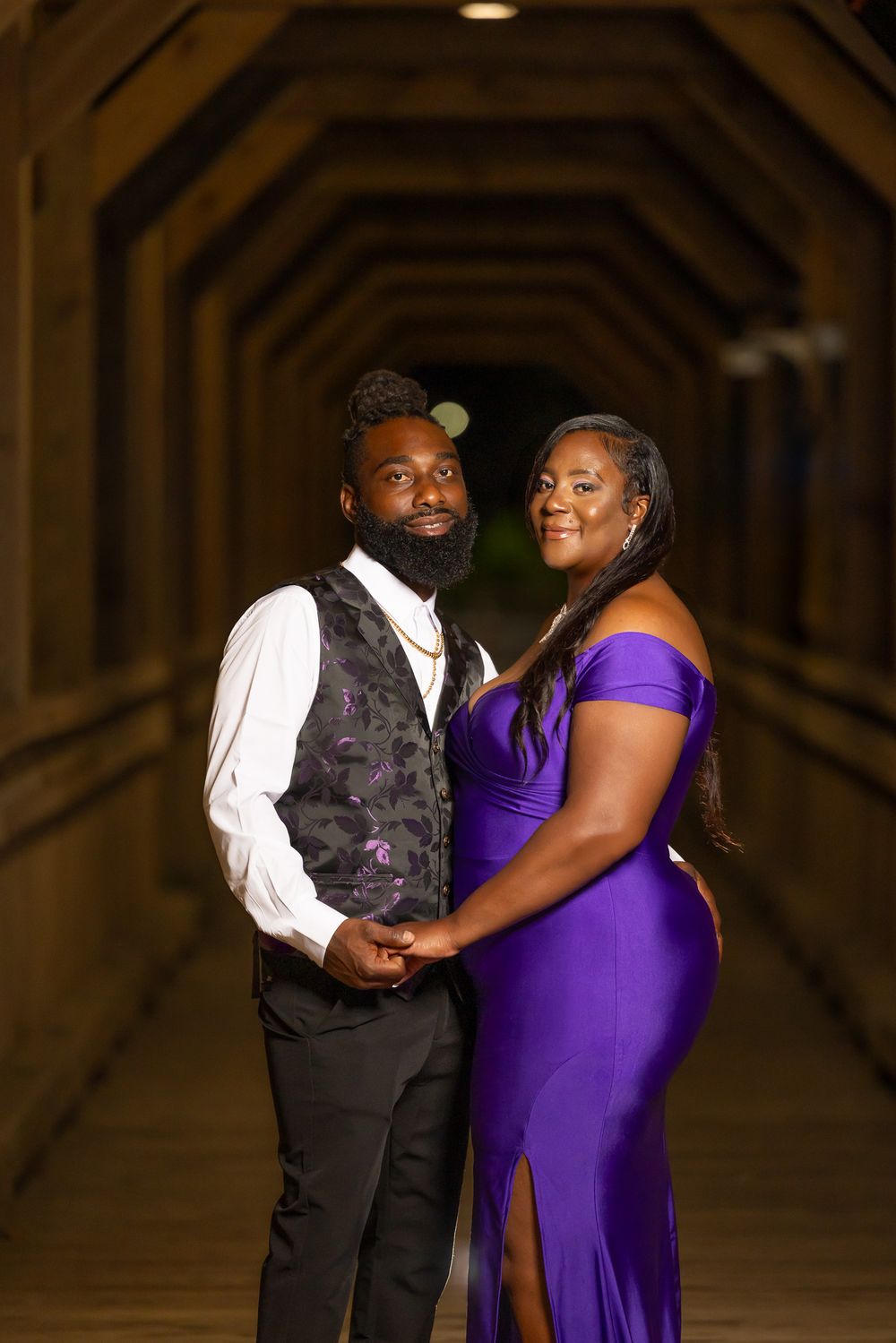 An intimate portrait of a couple in formal wear standing in a dimly lit wooden tunnel.