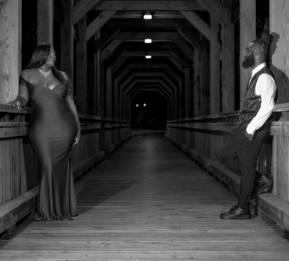 Black and white photo of a covered wooden walkway with dramatic lighting and two figures at different distances.