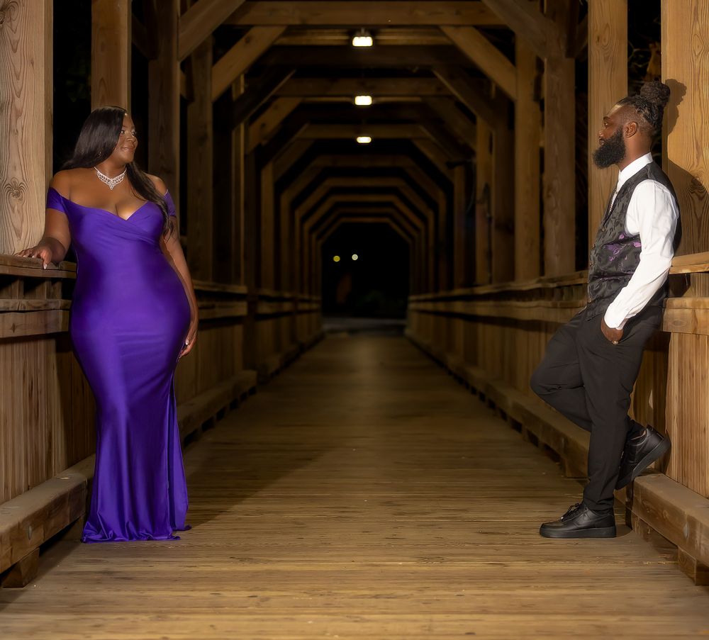 Wooden covered walkway with woman in purple dress and man in formal wear creating romantic atmosphere.