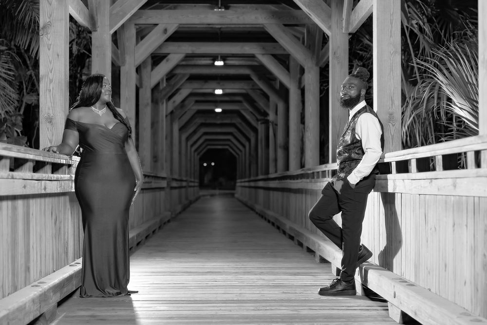 Long wooden covered corridor with dramatic lighting and formal-dressed figures creating striking shadows.