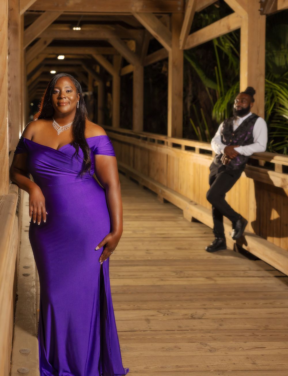 Photoshoot in wooden covered bridge walkway featuring purple evening gown and formal attire.