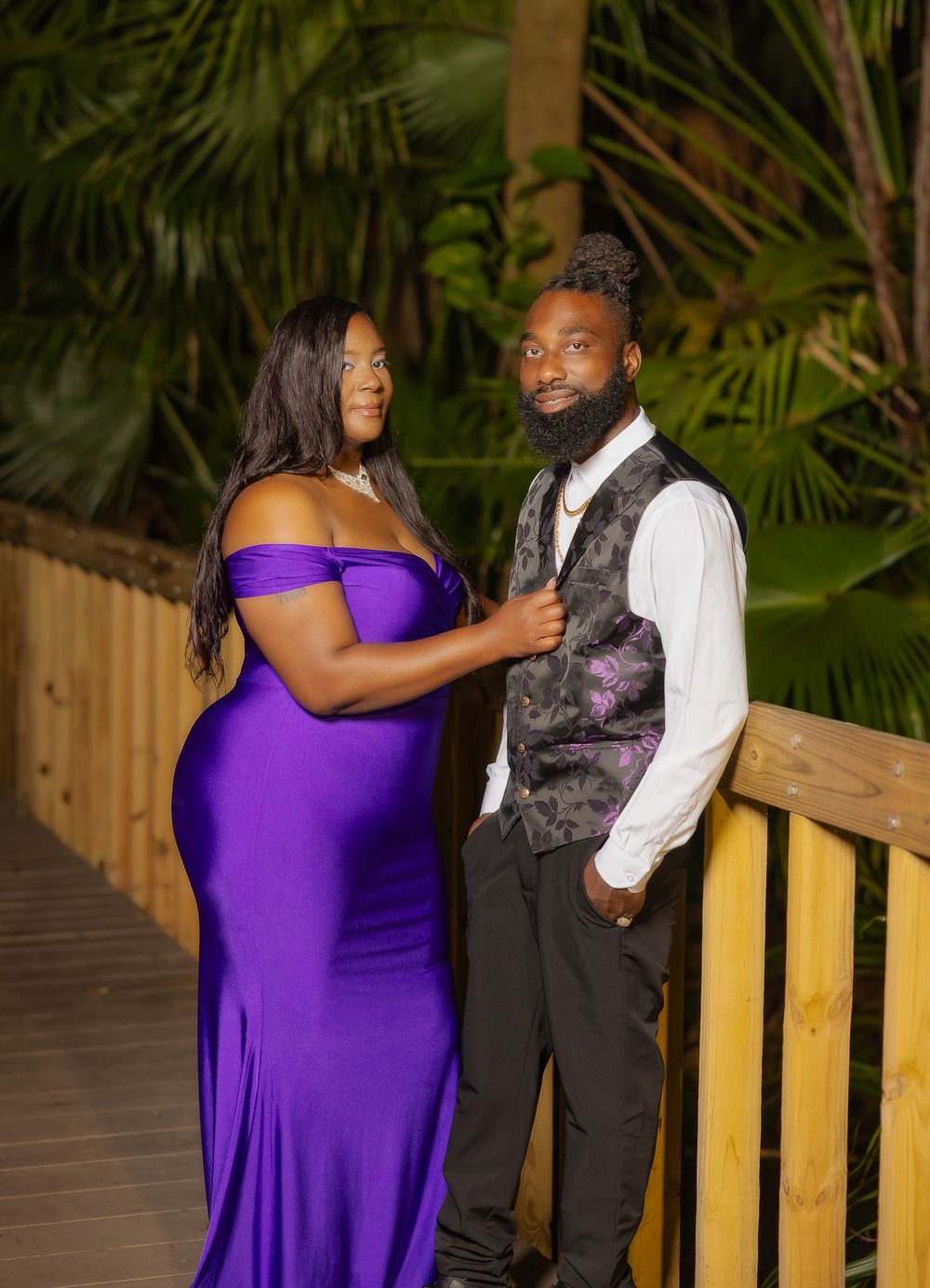 An intimate portrait of a couple in formal wear standing on a wooden deck surrounded by tropical foliage.