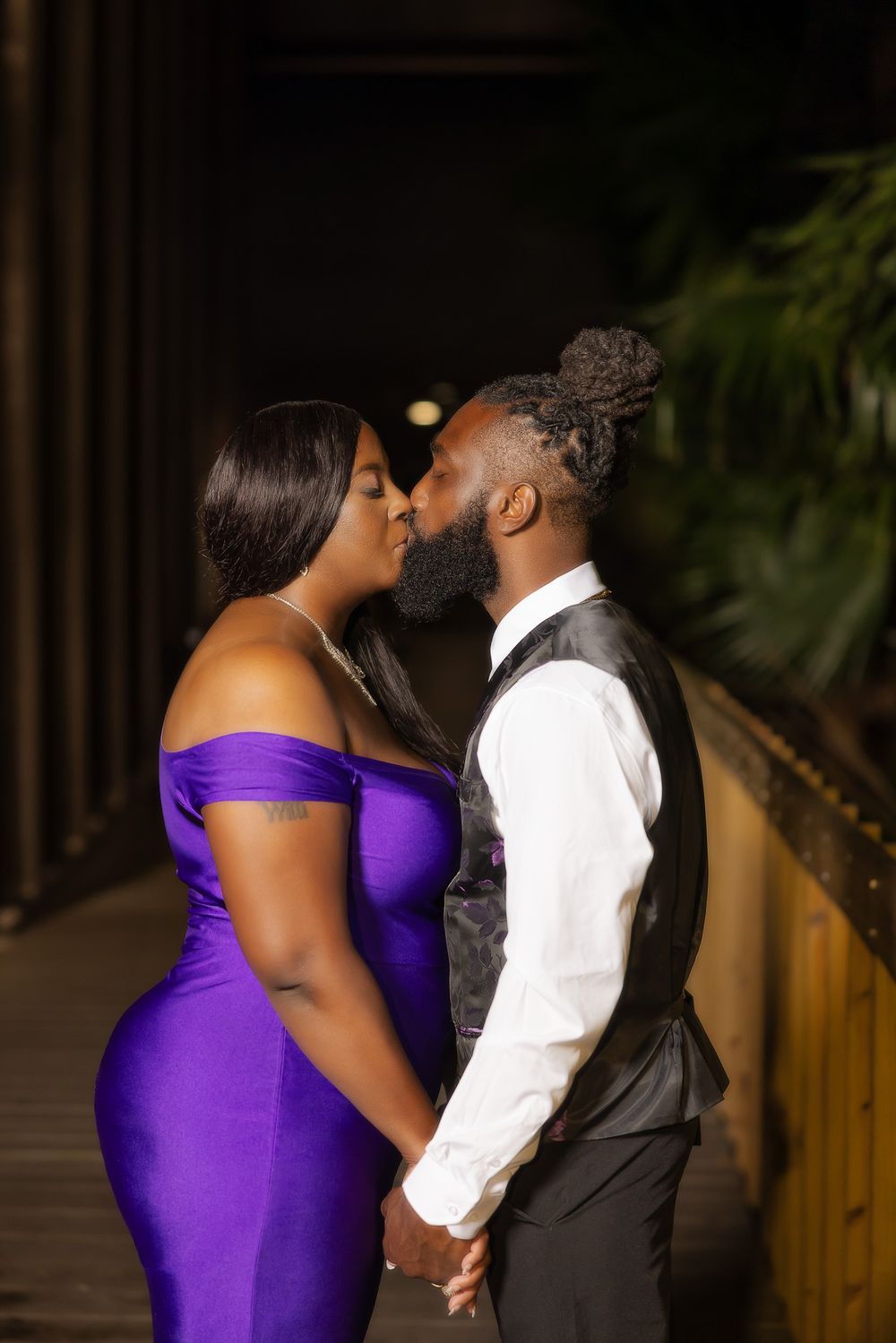 A tender moment shared between a couple in formal attire on a covered wooden walkway.