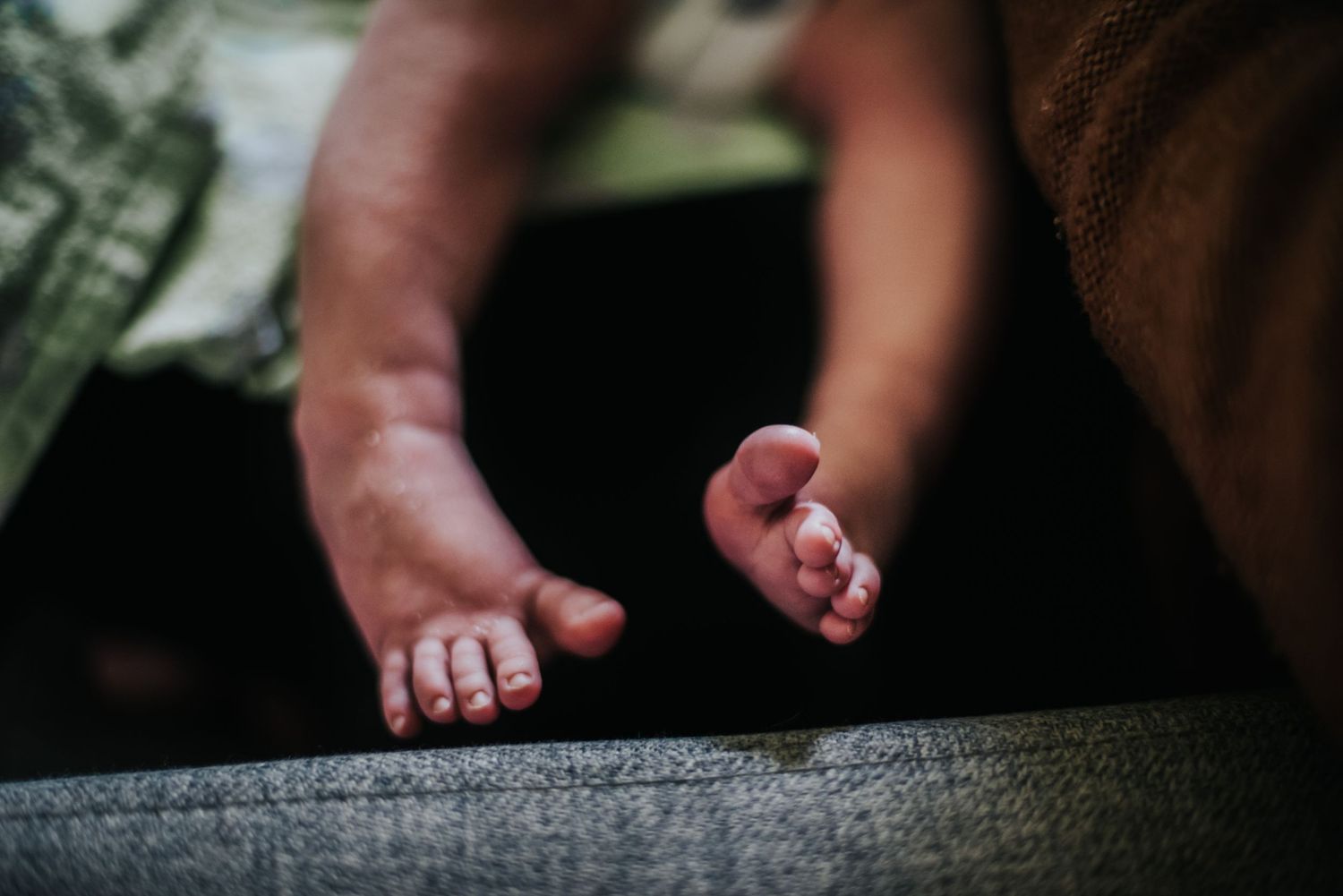 Close-up view of tiny baby feet with pink toes resting on a gray textile surface.