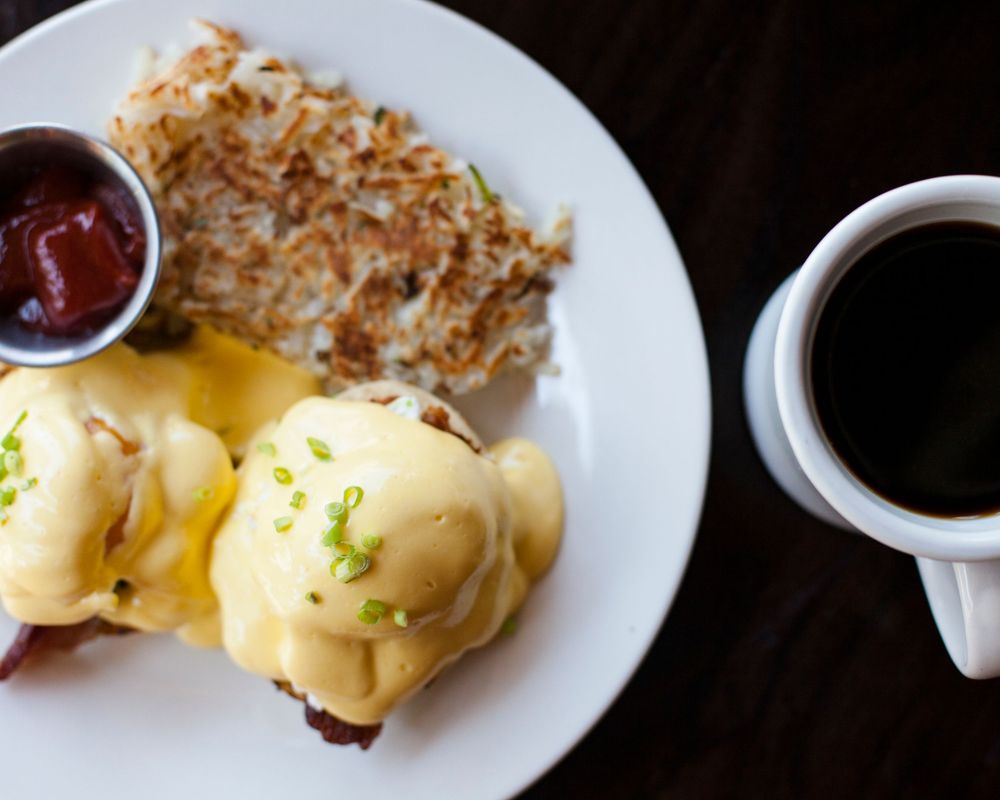 Close-up view of Eggs Benedict with hollandaise sauce drizzling over an English muffin on a white plate.