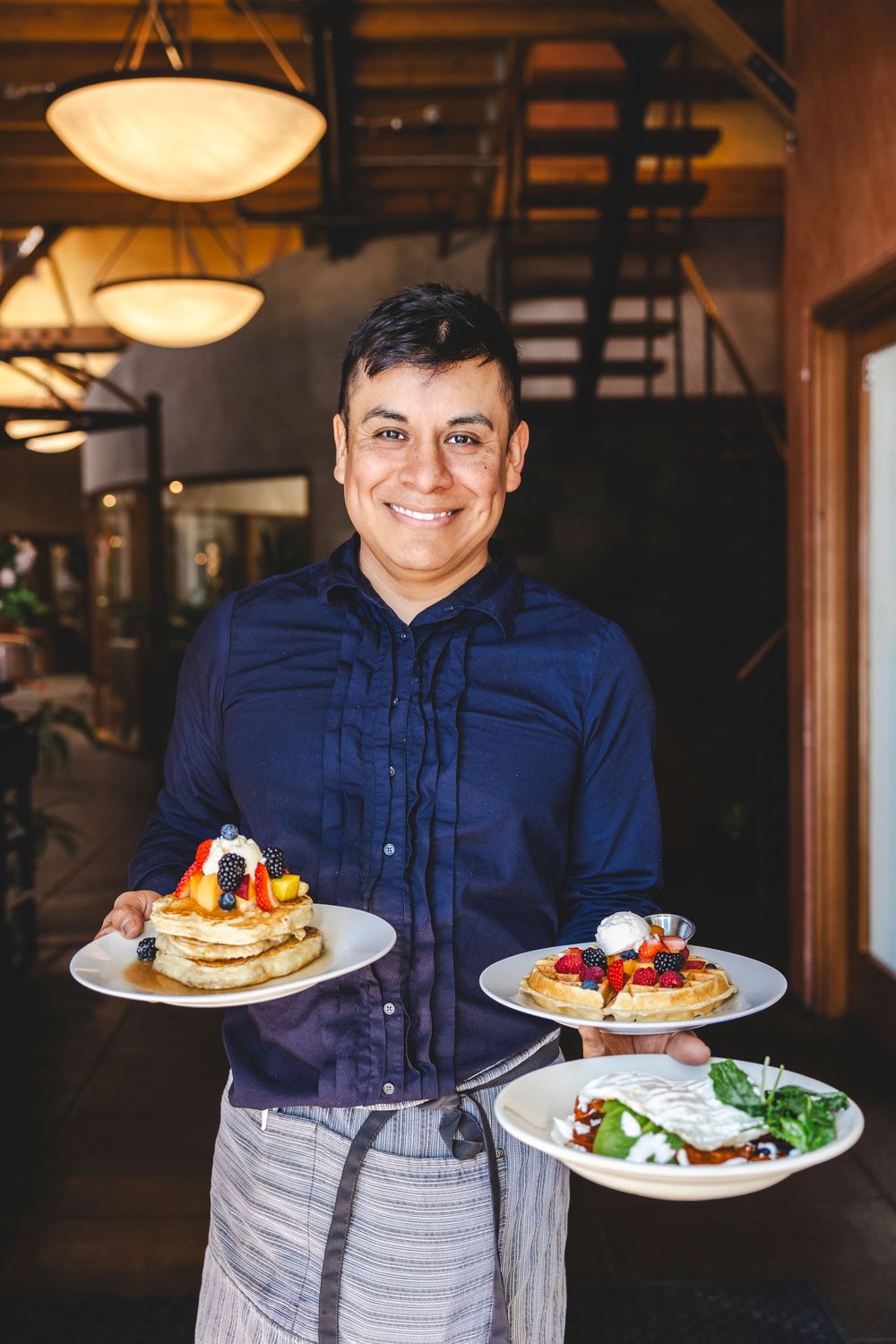 A server presents delicious plates of pancakes and salads in a warmly lit restaurant interior.