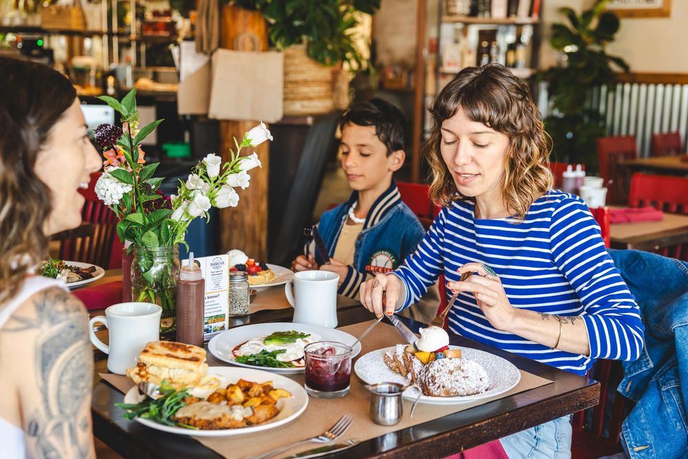 Diners enjoy a casual meal at a rustic restaurant with wooden tables and natural lighting.