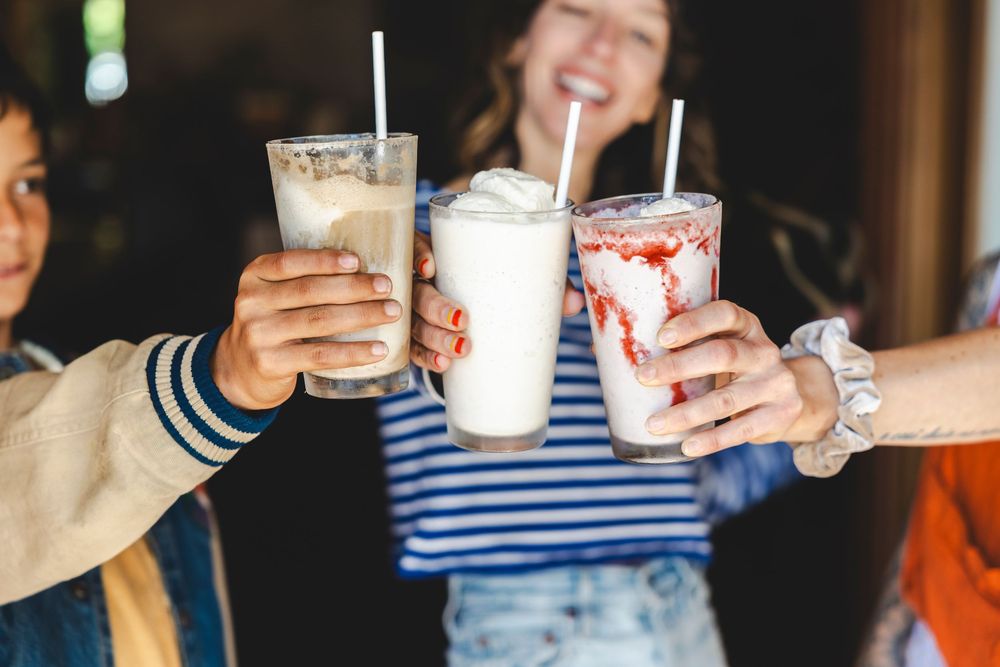 People holding milkshakes and beverages at a social gathering with striped shirts visible in the background.