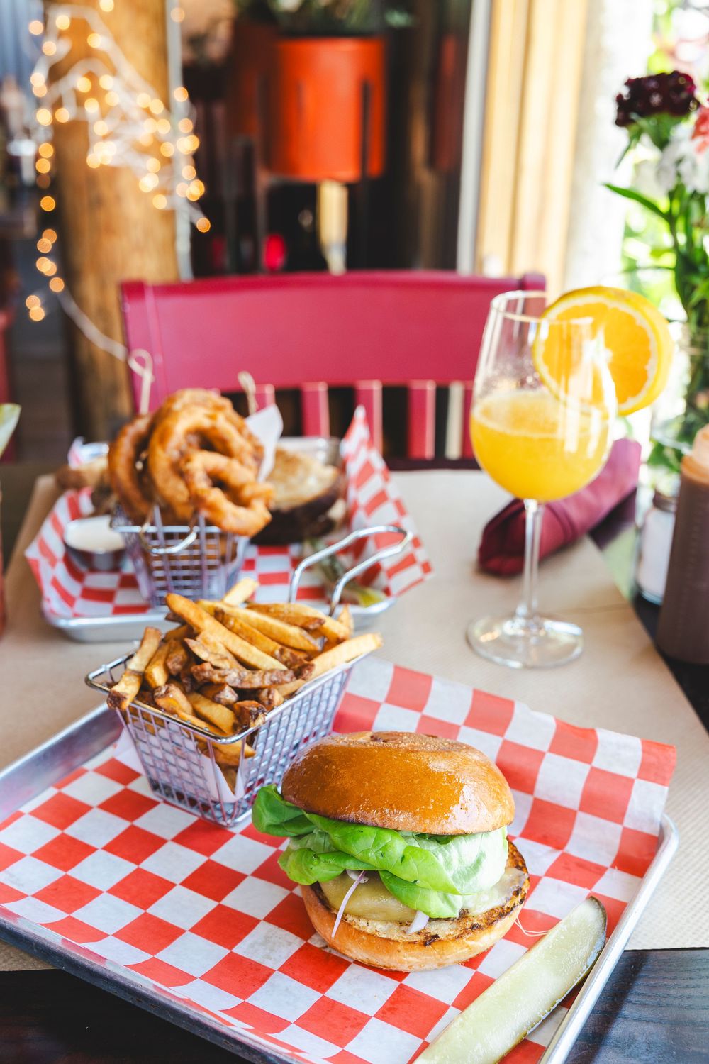 Classic burgers and crispy french fries served on red checkered paper in a diner setting with orange juice.