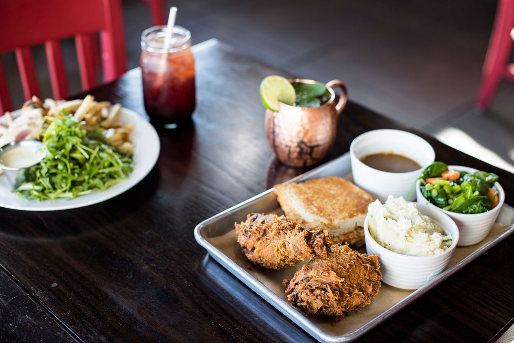 Restaurant platter with crispy fried food, sides of sauce and coleslaw, served with salad and cocktails on dark wooden table.