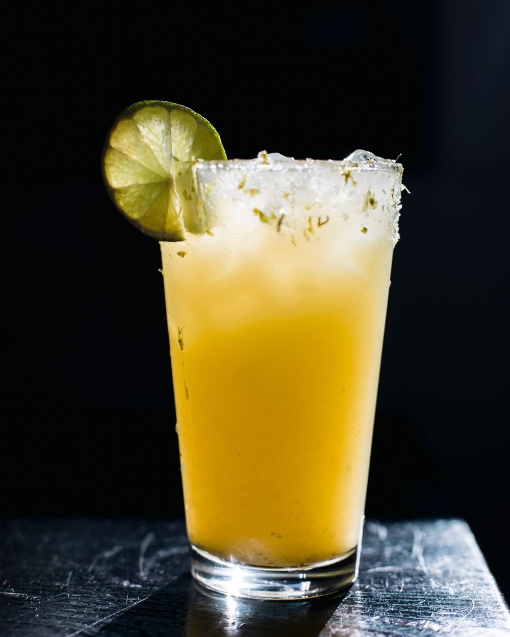 A refreshing citrus cocktail with lime garnish and salted rim served in a highball glass on a dark surface.