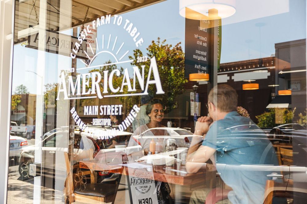A row of storefront windows displays AMERICANA branding with sunlit reflections and signage.