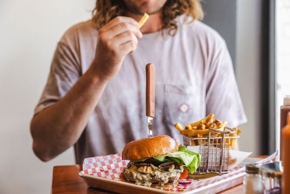 A pulled pork sandwich served on a brioche bun with crispy french fries in a metal basket on a wooden table.