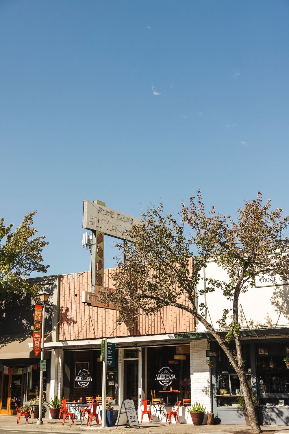 Modern strip mall retail storefront with wooden accents and outdoor seating area under clear blue skies.