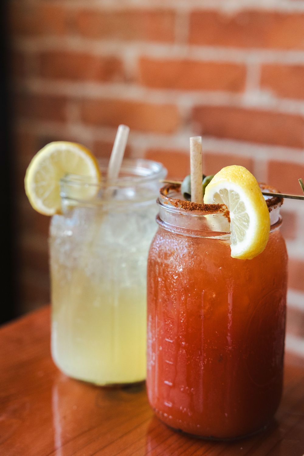 A row of refreshing cocktails with lemon garnishes served in glasses on a wooden surface against a brick wall background.