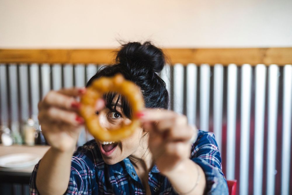 Someone playfully looks through a pretzel while wearing a blue denim shirt in a casual indoor setting.