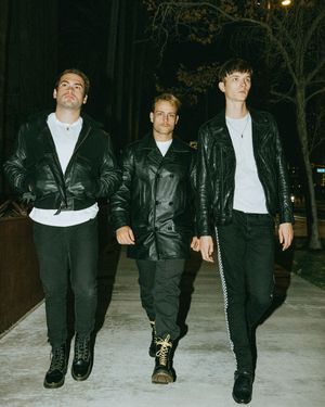 A group of people in black leather jackets and white shirts walk together on a snowy path at night.